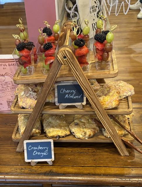 A wooden tiered tray of scones and fruit skewers with berries and grapes